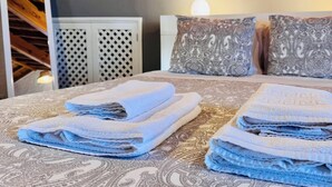 Un lit bien fait, avec des serviettes pliées, une literie à motifs et deux coussins décoratifs.