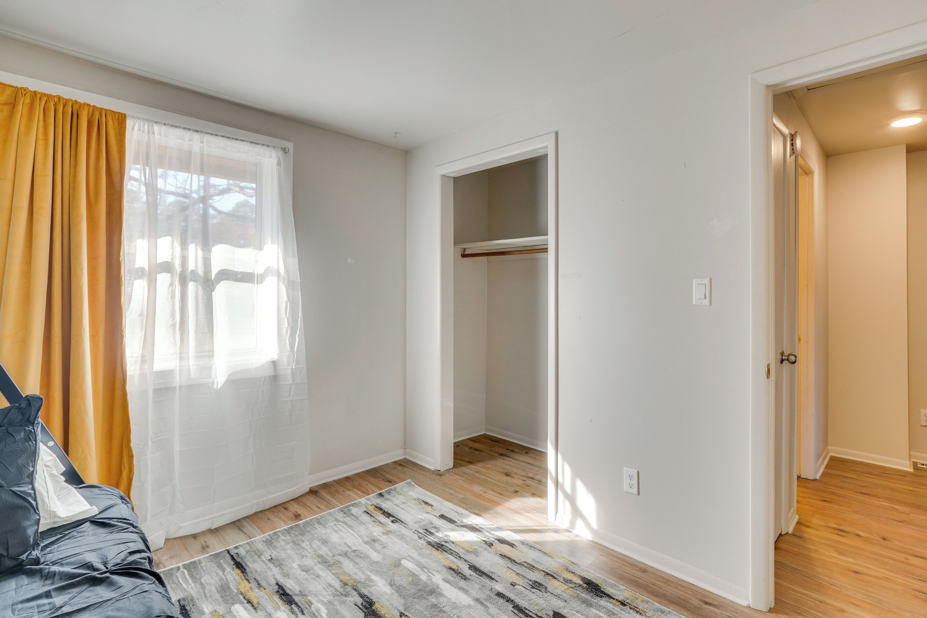 A room with a bed, a window with curtains, a closet, and a wooden floor.