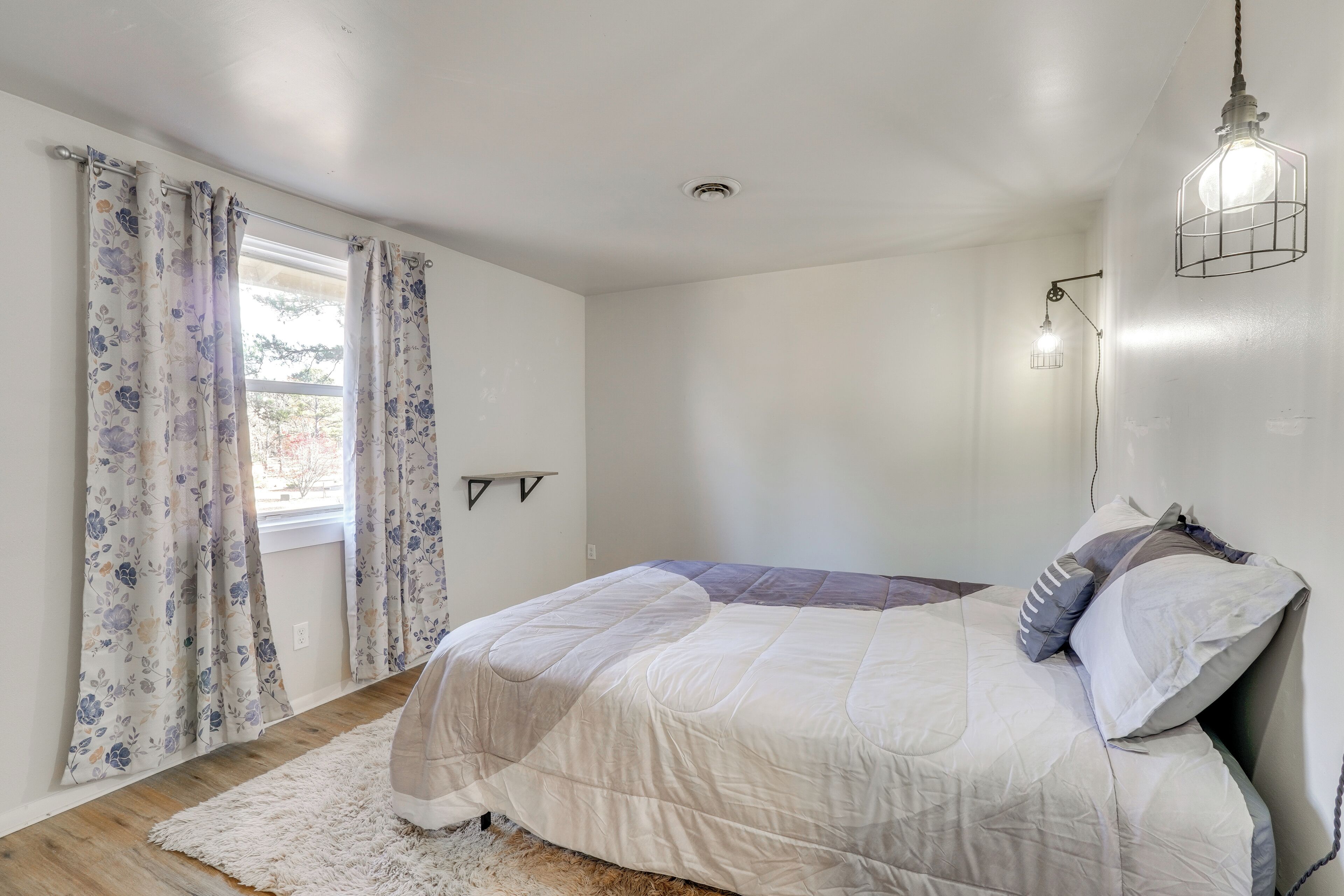 A bedroom with a bed, curtains, a rug, and a wall-mounted light fixture.