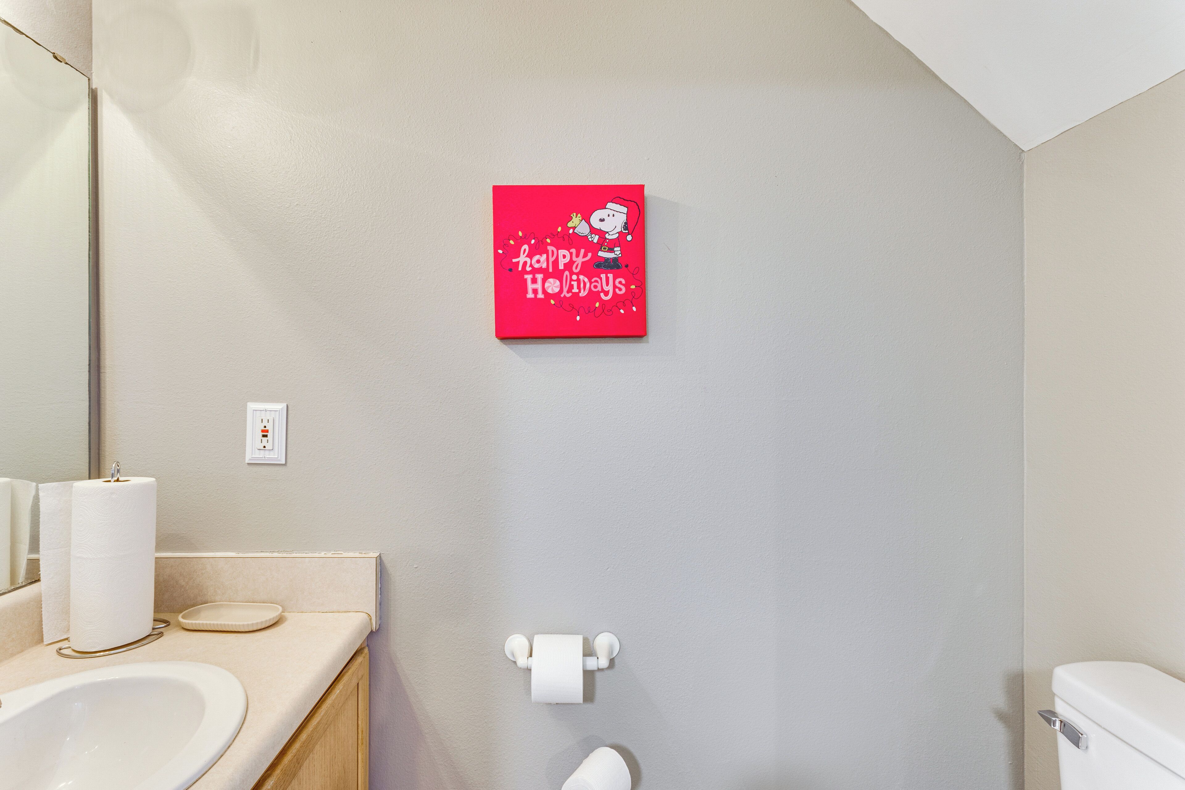 A bathroom with a toilet, sink, and a red holiday card on the wall.