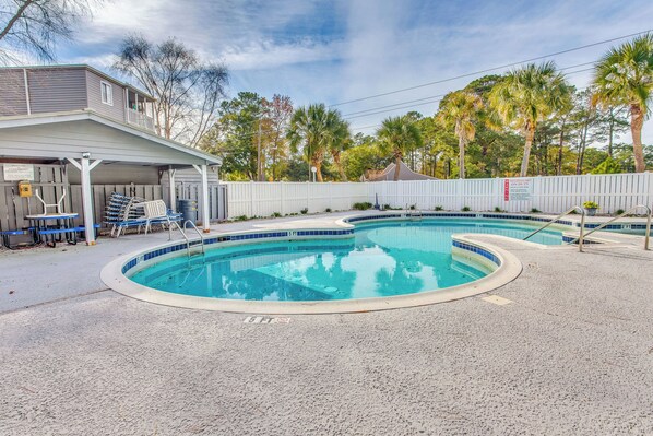 A swimming pool with a covered area, a fenced deck, and a building with a balcony.