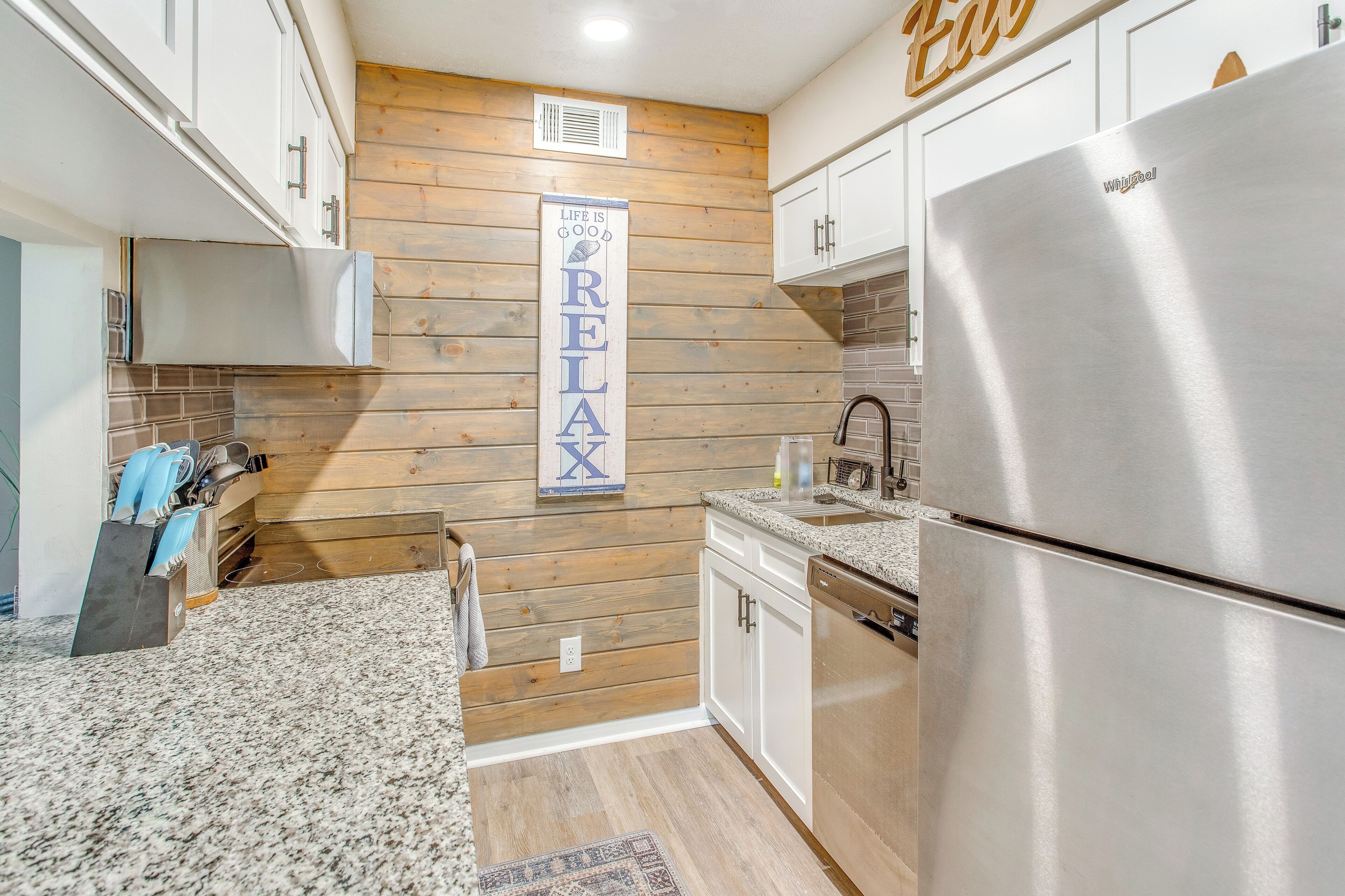 A modern kitchen with wooden panel walls, stainless steel appliances, and a 'RELAX' sign on the wall.