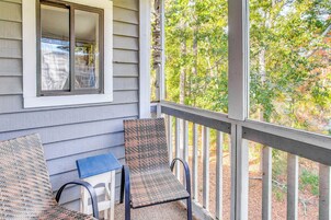 A porch with two wicker chairs and a small table, overlooking a wooded area.