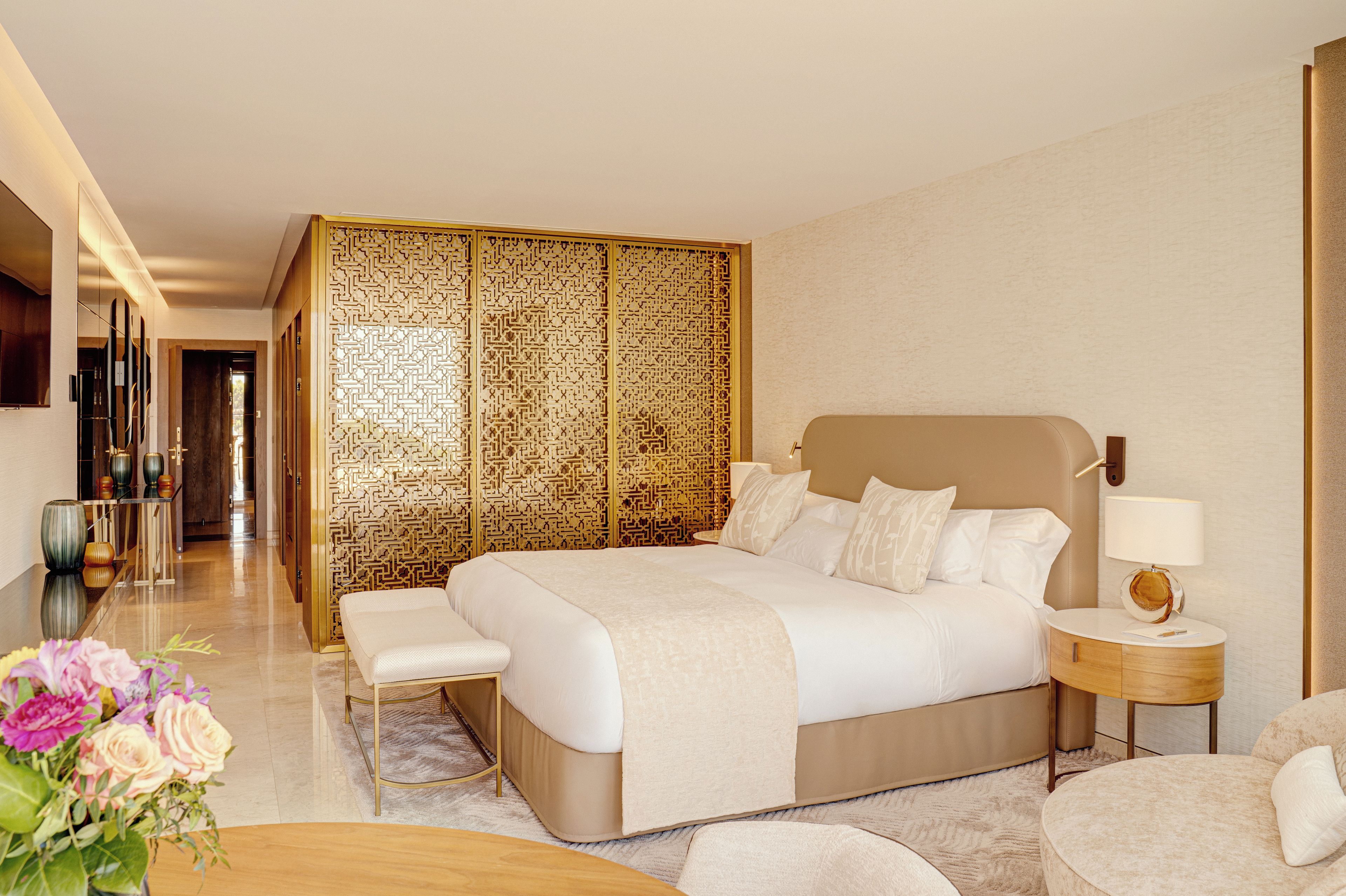 Una habitación de hotel moderna con una cama grande, mesitas de noche, una zona de estar y un separador decorativo.