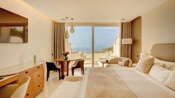 A hotel room with a bed, a desk, a chair, a table, and a view of the sea.