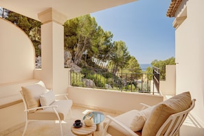 A balcony with white furniture, a small table with a teapot and cup, and a view of trees and the sea. - ZEM Wellness Clinic Altea - 5 Stars Grand Luxury (Altea)
