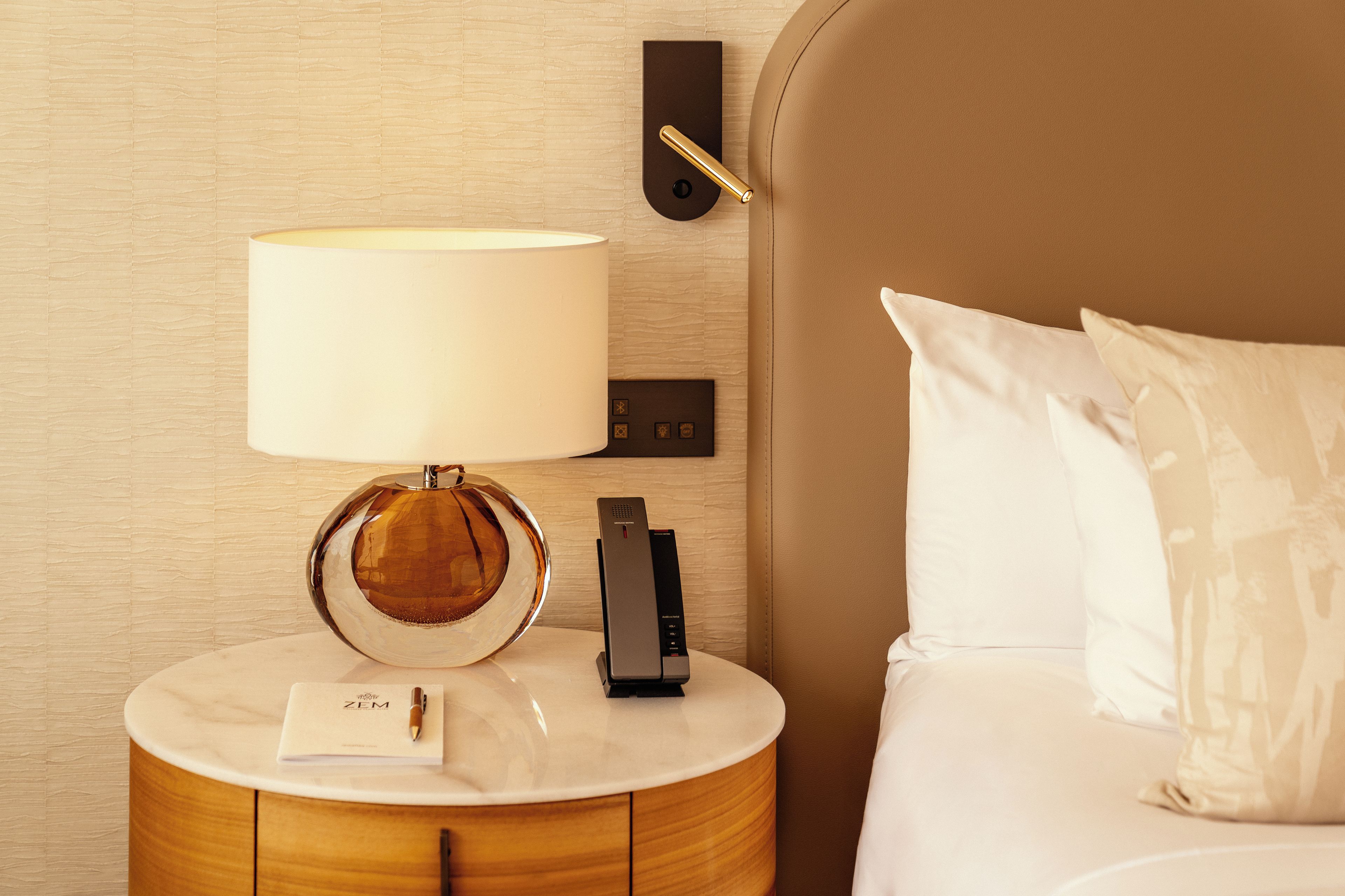 Une chambre d’hôtel avec un lit, une table de chevet avec une lampe, une télécommande et une carte posée sur la table.