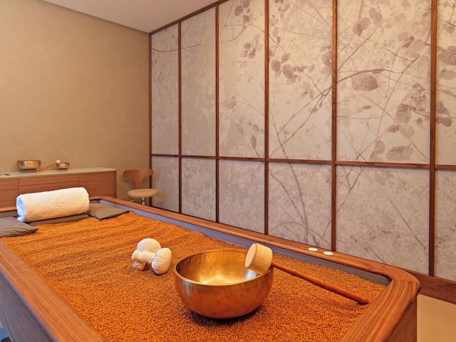 Una habitación con una mesa de masaje de madera, un tazón metálico grande y un mazo de madera.
