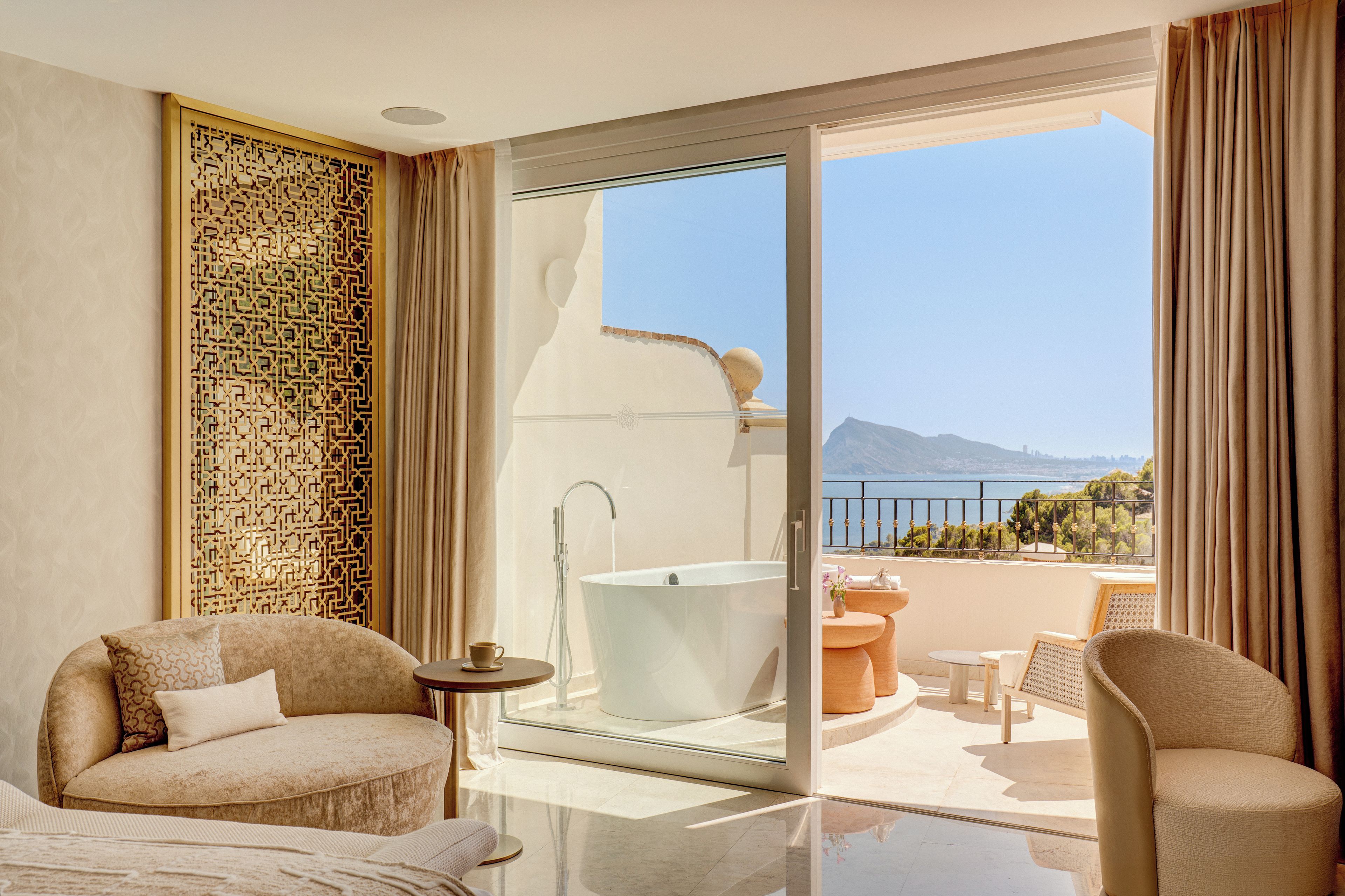 Uma casa de banho moderna com uma banheira independente, um chuveiro com parede de vidro e vista para o mar.