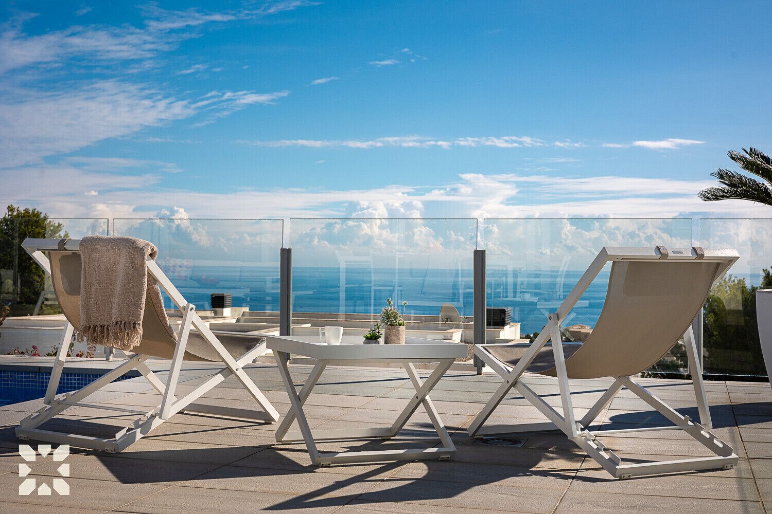 A rooftop terrace with two lounge chairs, a small table, and a view of the ocean.