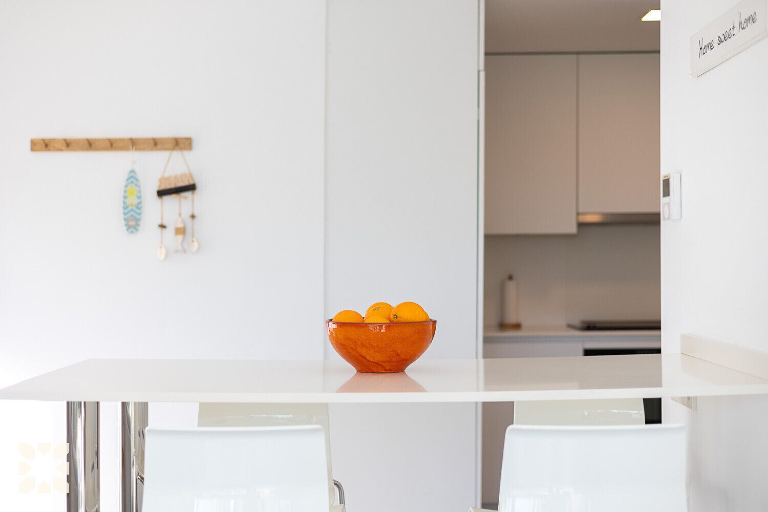 Eine moderne Küche mit weißen Schränken, eine Glasbowl mit Orangen auf der Arbeitsfläche und ein Schild mit der Aufschrift 'Home sweet home' an der Wand.