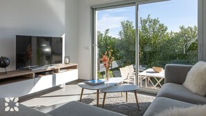 A modern living room with a flat-screen TV, a coffee table, and a sofa. There is a sliding glass door leading to an outdoor patio area with a table and chairs. - Villa YANSA by Abahana Villas (Benitachell)