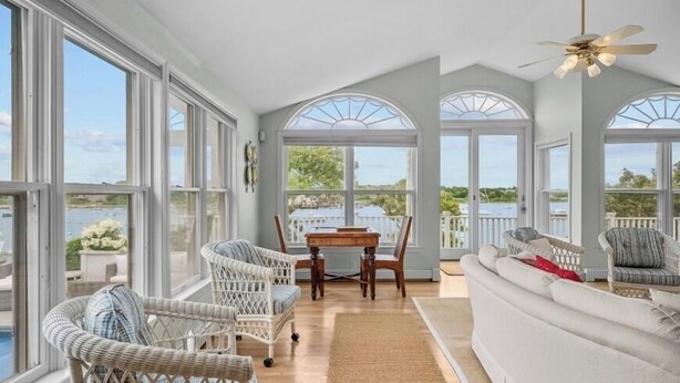 A spacious sunroom with large windows, wicker furniture, a white sofa, and a dining table.