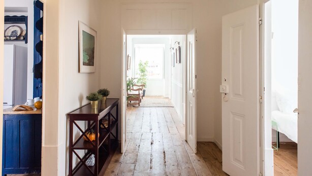 A hallway with wooden flooring, a dark wooden console table with decorative items, and a white door on the right.