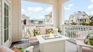 Un balcón con sofá blanco, una mesa de vidrio con chimenea y vistas a casas vecinas.
