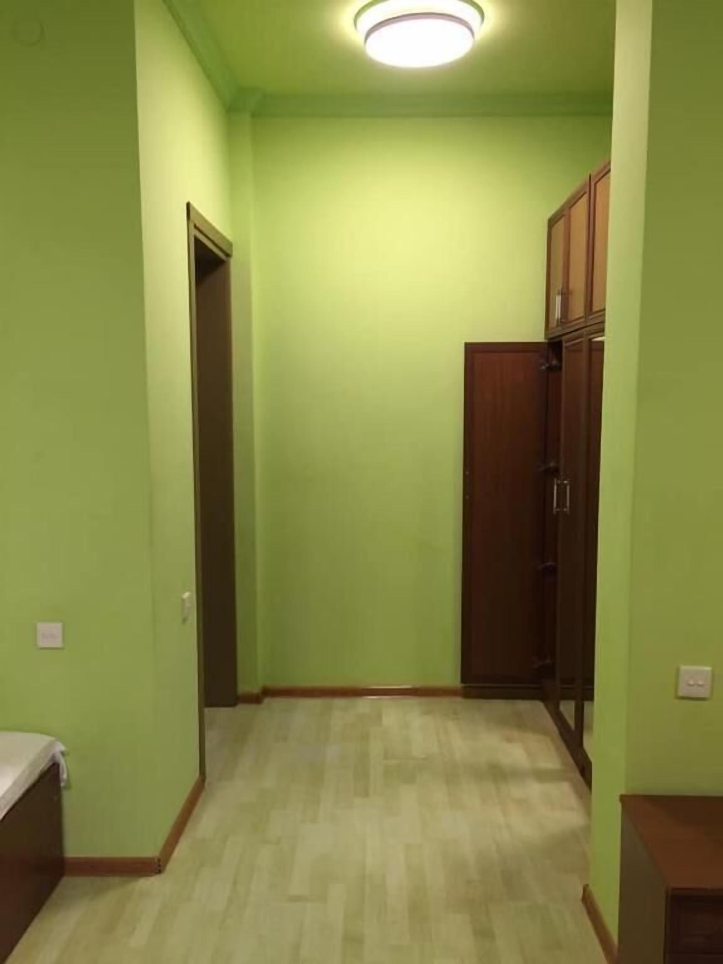 A room with green walls, a wooden floor, and a ceiling light.
