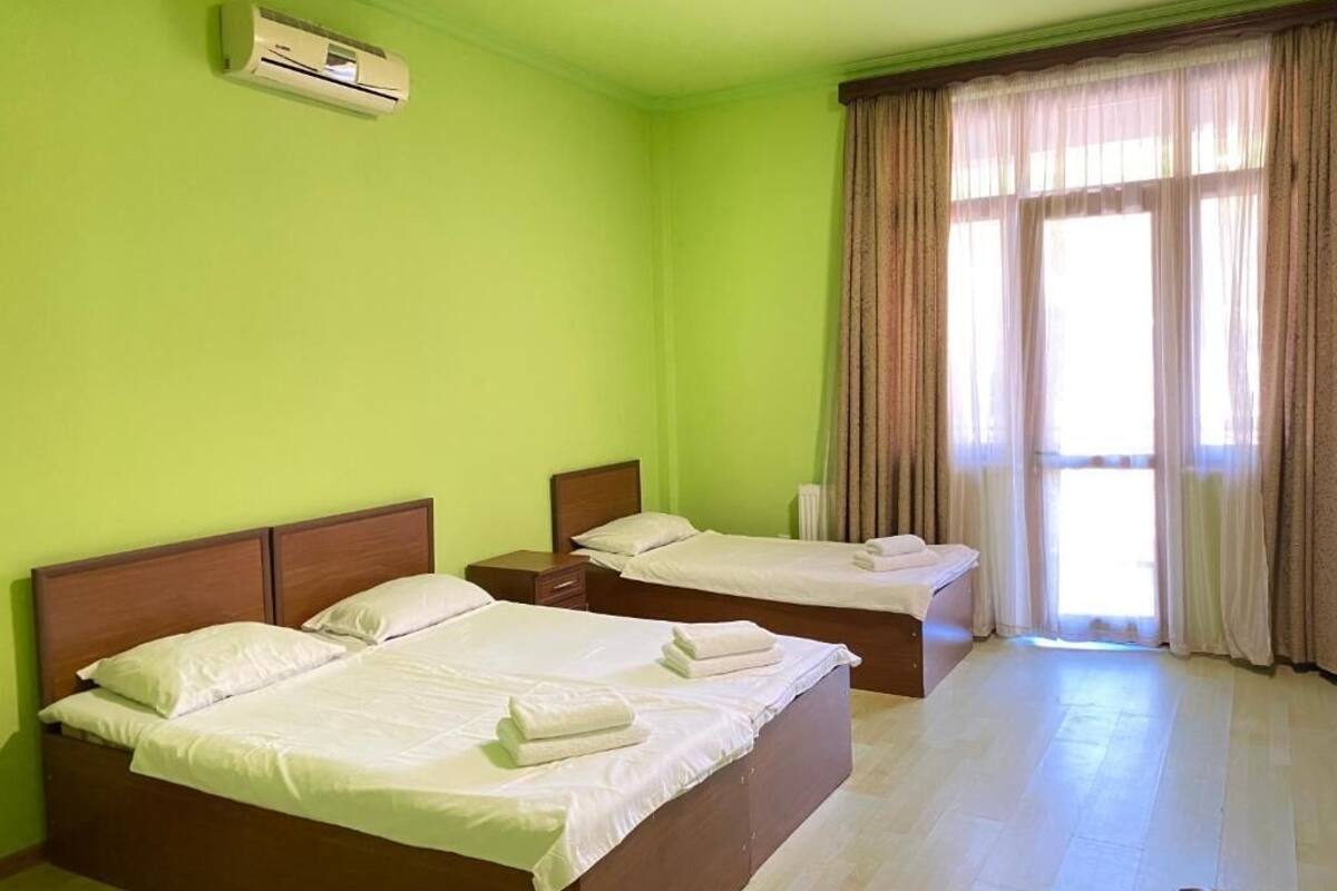 A hotel room with two beds, a window with curtains, and an air conditioning unit on the wall.