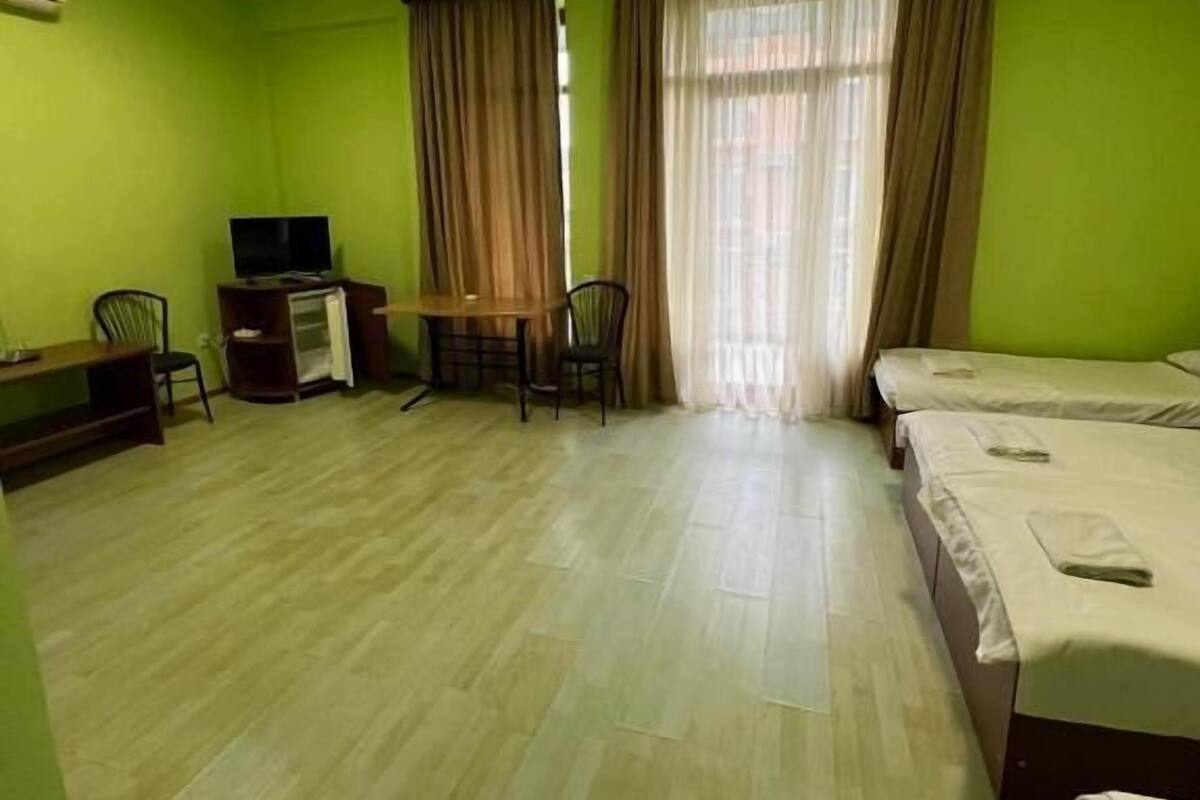 A hotel room with a bed, a desk with a chair, a television, and a window with curtains.