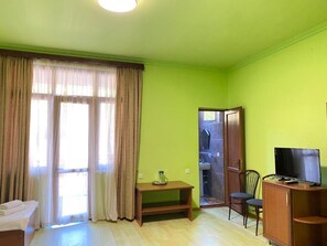 A room with a green wall, a bed, a TV, a desk, and a bathroom door. - MARETI HOTEL (Batumi)