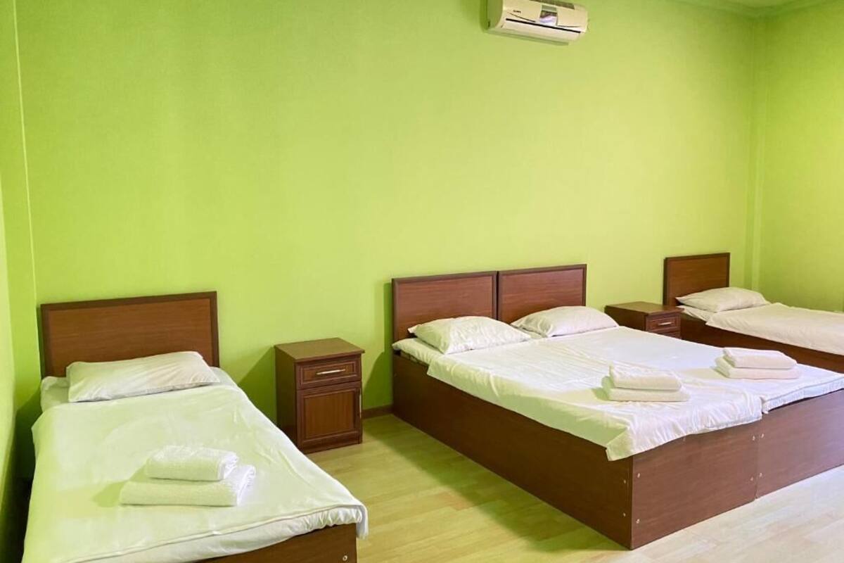 A hotel room with three single beds, each with a wooden headboard and white bedding. There is a small wooden nightstand with a drawer next to each bed.