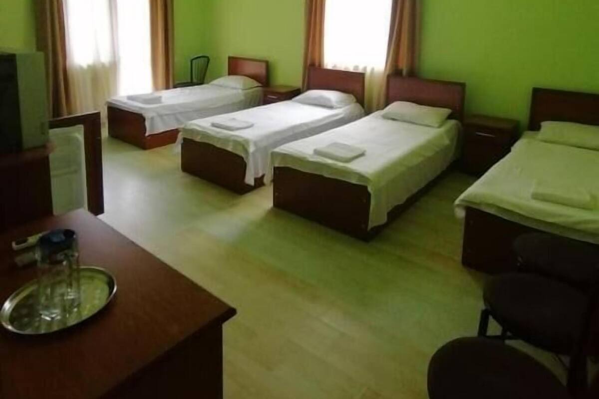 A hotel room with four single beds, a desk with a chair, and a TV.