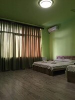 Una habitación con dos camas, una lámpara en el techo, una ventana con cortinas y un equipo de aire acondicionado.