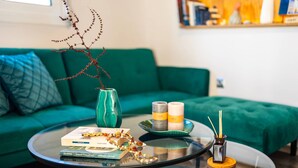 Ein Wohnzimmer mit einem grünen Sofa, einem Glastisch mit Büchern, Kerzen und einem dekorativen Ast.