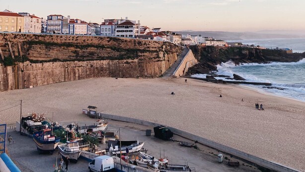 Eine Küstenstadt mit Sandstrand, einer Klippe und einer Uferpromenade mit Booten und Fahrzeugen.