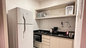 Eine moderne Küche mit einem weißen Kühlschrank, einer Mikrowelle, einem Herd und einem eingebauten Backofen. Ein Spülbecken mit Wasserhahn ist vorhanden, darüber eine Ablagefläche mit Gläsern und einem Wasserspender.