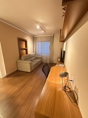 A modern living room with a wooden desk, a sofa, and a large window with sheer curtains. - Victoria Charm Stylish 1 BDR in Itaim Bibi (São Paulo)