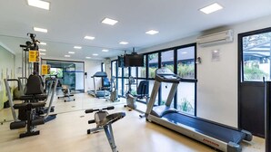 Ein Fitnessstudio mit verschiedenen Trainingsgeräten, großen Fenstern und einem Laufband.