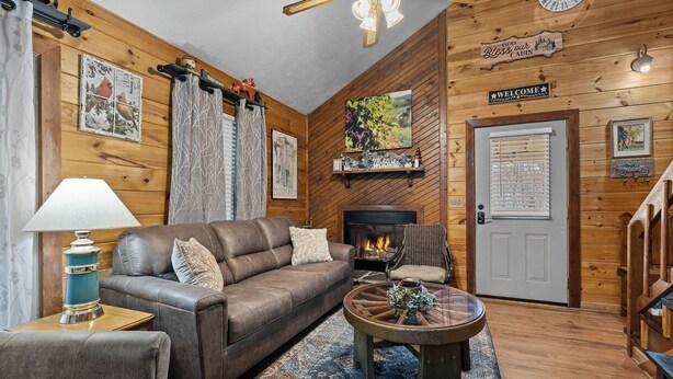 A cozy cabin interior with a leather sofa, a round coffee table, a fireplace, and wooden walls. - New Listing! Hot Tub, Foosball, Fireplace, Pool Table, & Free Attractions! (Sevierville)