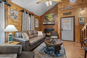 A cozy cabin interior with a leather sofa, a round coffee table, a fireplace, and wooden walls. - New Listing! Hot Tub, Foosball, Fireplace, Pool Table, & Free Attractions! (Sevierville)