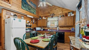A wooden cabin-style kitchen with a dining table set for four, wooden cabinets, a refrigerator, and a ceiling fan. - New Listing! Hot Tub, Foosball, Fireplace, Pool Table, & Free Attractions! (Sevierville)