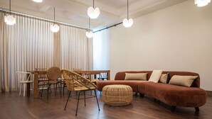 A modern living room with a brown sofa, wicker chairs, a dining table, and pendant lights. - Liiiving in Porto - Casa Duque Apartment I (Porto)