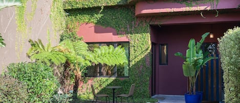 A courtyard with a round table and chairs, surrounded by lush greenery and a large potted plant.