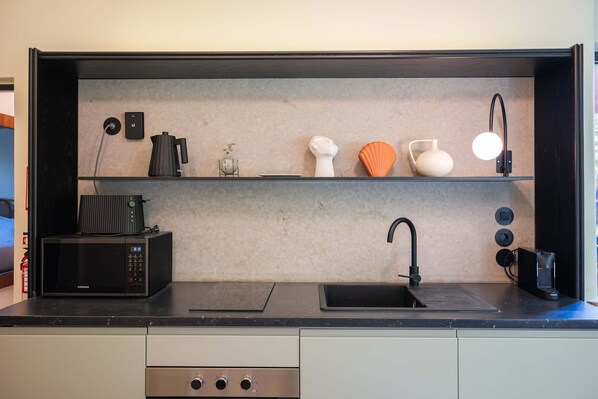 A modern kitchen with a black countertop, a built-in microwave, a sink, and a shelf with decorative items. - Liiiving in Porto - Casa Duque Apartment I (Porto)