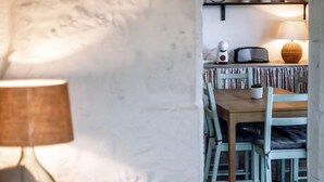 A cozy living room with a sofa and a lamp, leading to a dining area with a table and chairs. - Liiiving in A Ores - Ocean View House (Sao Roque do Pico)