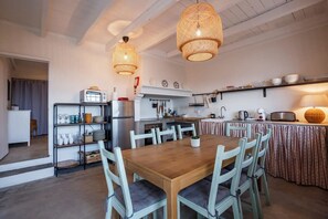A kitchen with a wooden table and chairs, a refrigerator, and hanging wicker light fixtures. - Liiiving in A Ores - Ocean View House (Sao Roque do Pico)