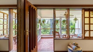 A room with a wooden door leading to a balcony with a view of greenery. - Lazy Days (Diani Beach)