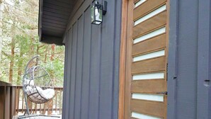 A wooden door with horizontal slats, a porch with a swing chair, and a welcome mat. - Beautiful Renovated Cozy Forest Home in Crestline with Hot Tub (Crestline)