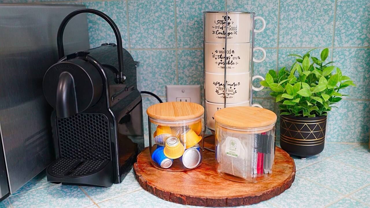 Una encimera de cocina con una máquina para gofres, una pila de latas y una planta en maceta.