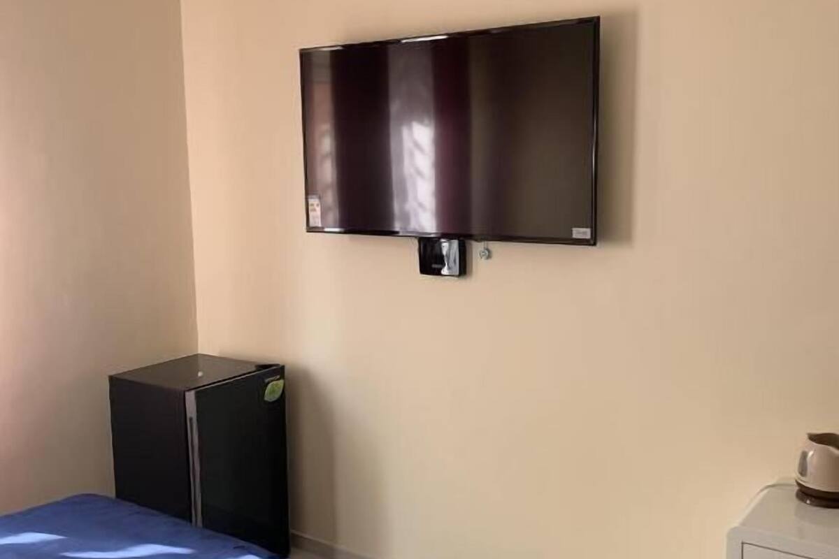 A hotel room with a bed, a television mounted on the wall, a small desk, and a trash bin.