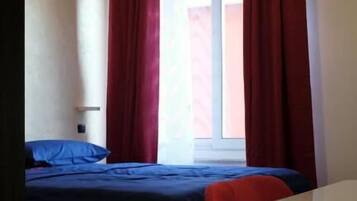 Une chambre à coucher avec un lit, une fenêtre avec des rideaux rouges et une table de chevet blanche.