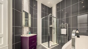 Ein modernes Badezimmer mit einer gläsernen Dusche, einem lila Waschtisch und einer weißen Badewanne.