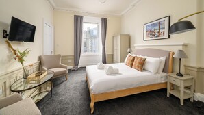 Ein Hotelzimmer mit Bett, Fernseher, Schreibtisch, Stuhl, Lampe und einem Fenster mit Vorhängen.