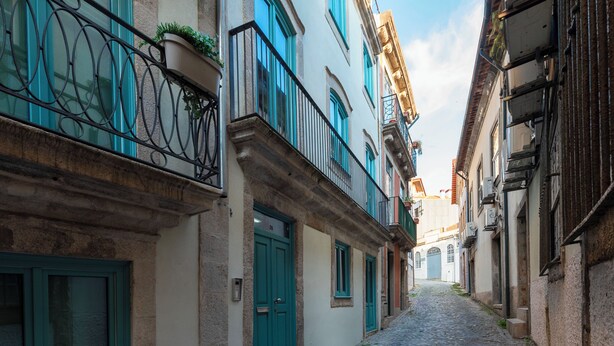 A narrow cobblestone street flanked by buildings with balconies and doors. - Unusual House (Porto)