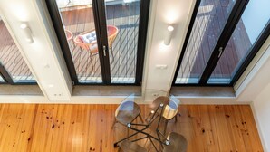 A modern interior with a wooden floor, a glass table with chairs, and large windows overlooking an outdoor area with a wooden deck and chairs. - Unusual House (Porto)