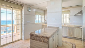 Une cuisine spacieuse avec un grand îlot central, donnant sur l’extérieur, et un balcon avec vue sur la mer.