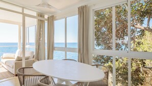 Une pièce dotée d’une grande fenêtre donnant sur la mer, d’une table ronde entourée de chaises et d’un canapé agrémenté de coussins.